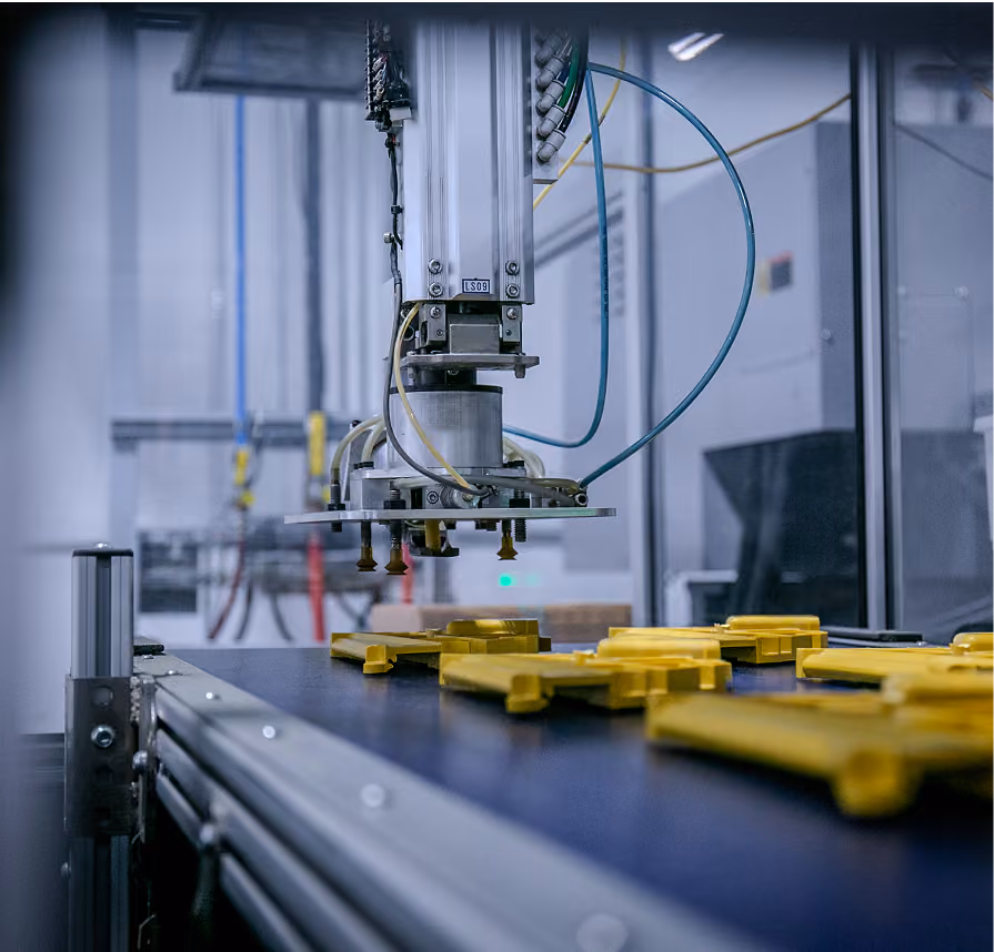 Robotic arm with attached suction cups positioned above a conveyor belt with yellow plastic parts in a manufacturing or assembly line setting.