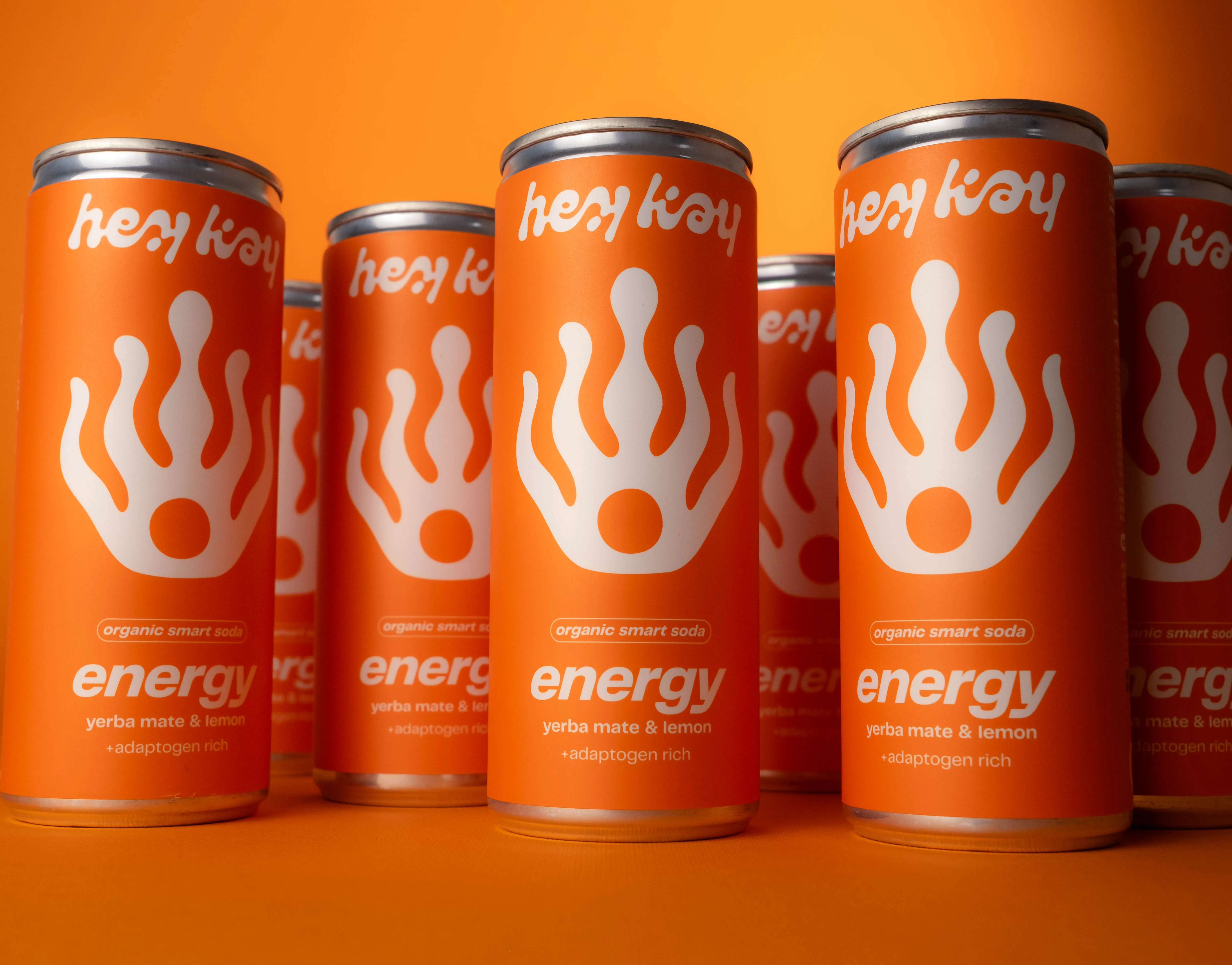 Latas de hey kay energy, refrigerante com erva-mate e limão, em fundo laranja