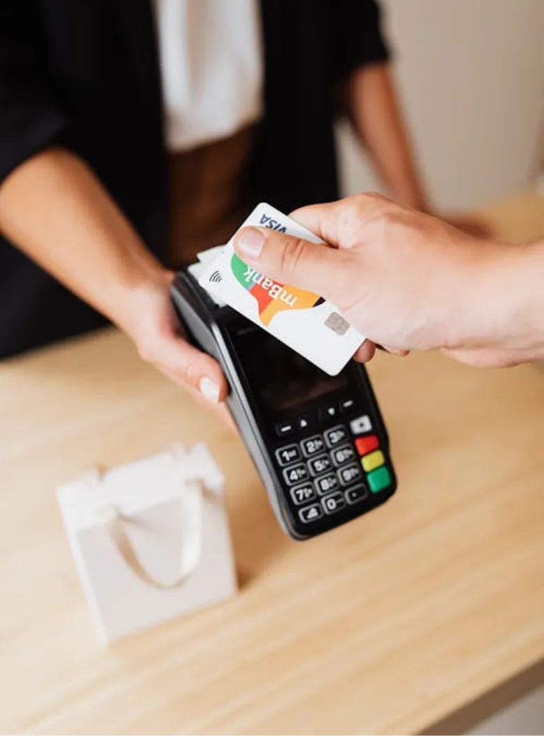 Person making a contactless payment with a credit card on a card reader held by another person.