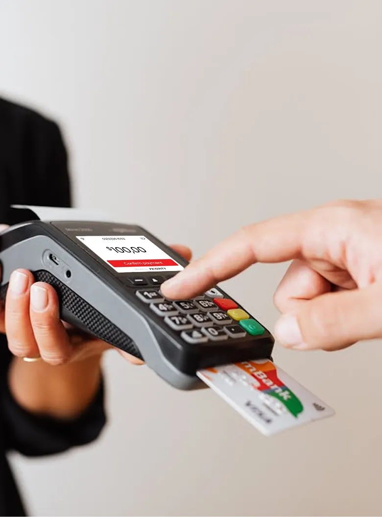 Person holding a payment terminal while another hand presses a button, with a bank card inserted and screen showing $100.00 payment.