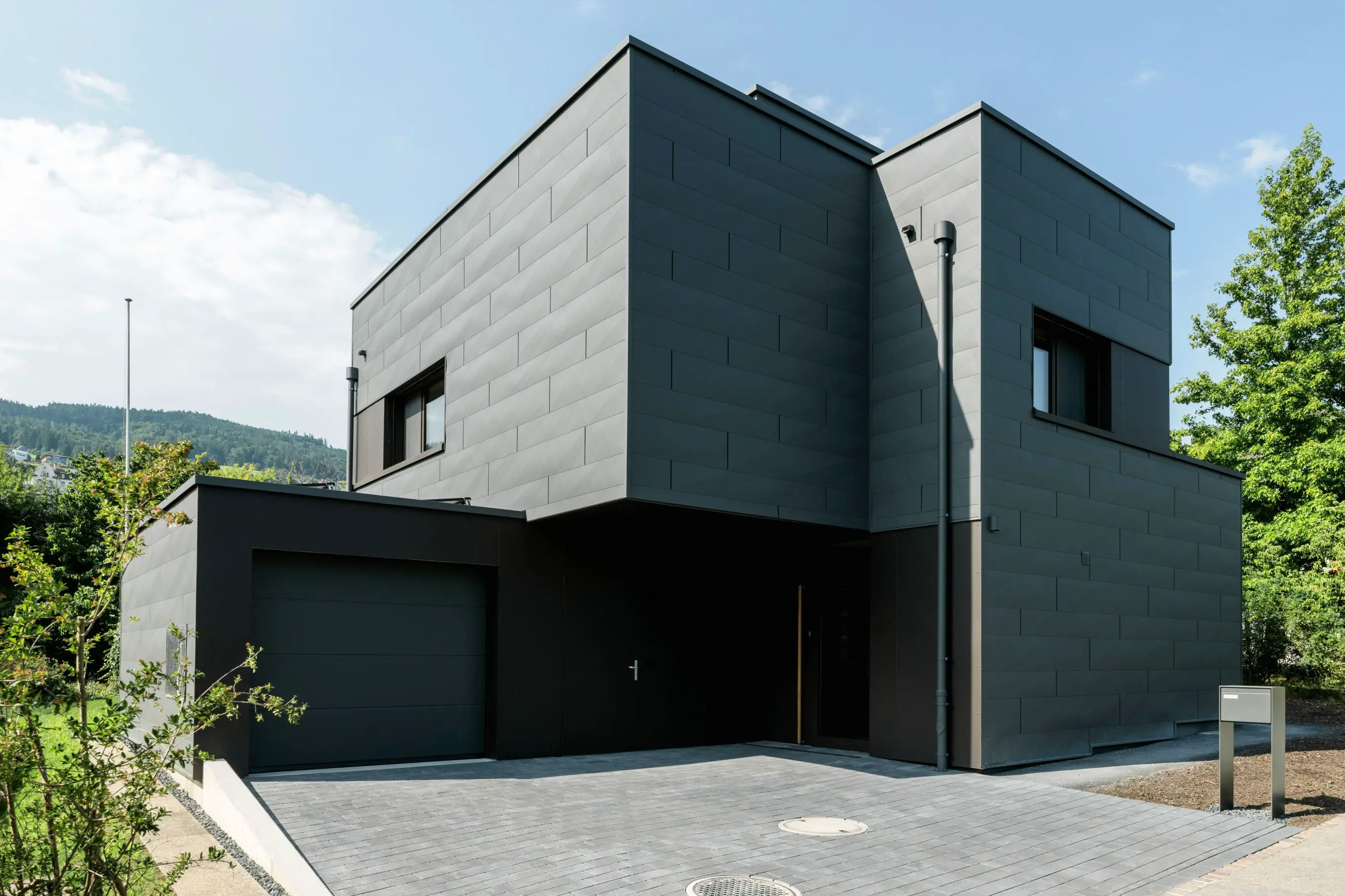 Modernes zweistöckiges Haus mit dunkler Fassade, großer Garage und gepflegter Einfahrt.