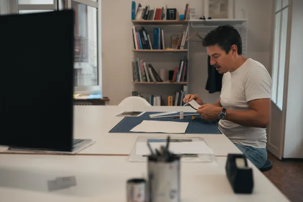 Mann sitzt an einem Tisch und arbeitet an einem Design in einem Büro mit Bücherregal.