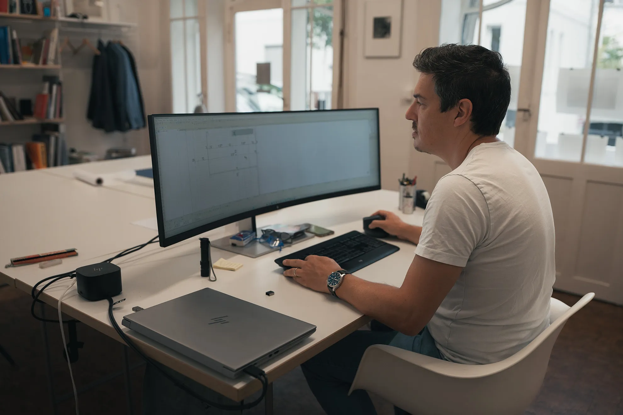 Mann arbeitet an technischem Zeichnungsentwurf auf großem gebogenen Monitor am Schreibtisch.
