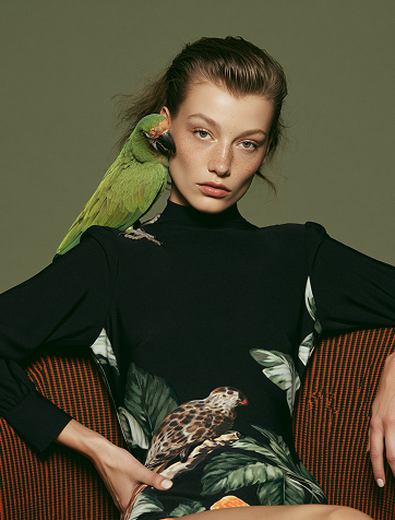 Portrait of a woman with a green parakeet perched on her shoulder, wearing a botanical-print dress