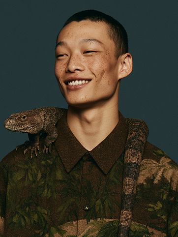 Portrait of a smiling man with a lizard perched on his shoulder, wearing a tropical-print shirt