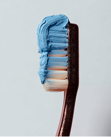 Close-up of a toothbrush with blue toothpaste on its bristles against a plain background.