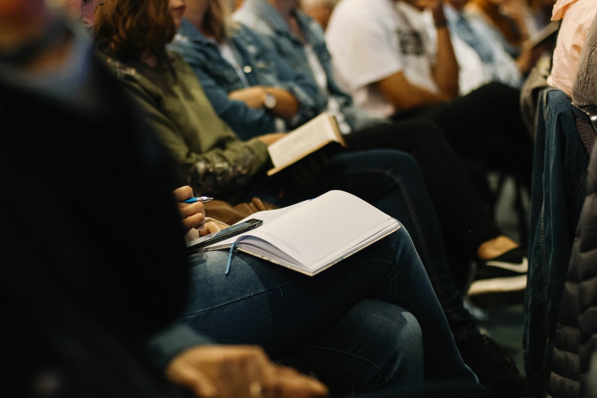 People sitting closely in a row with jeans, one holding a pen and an open notebook on their lap.