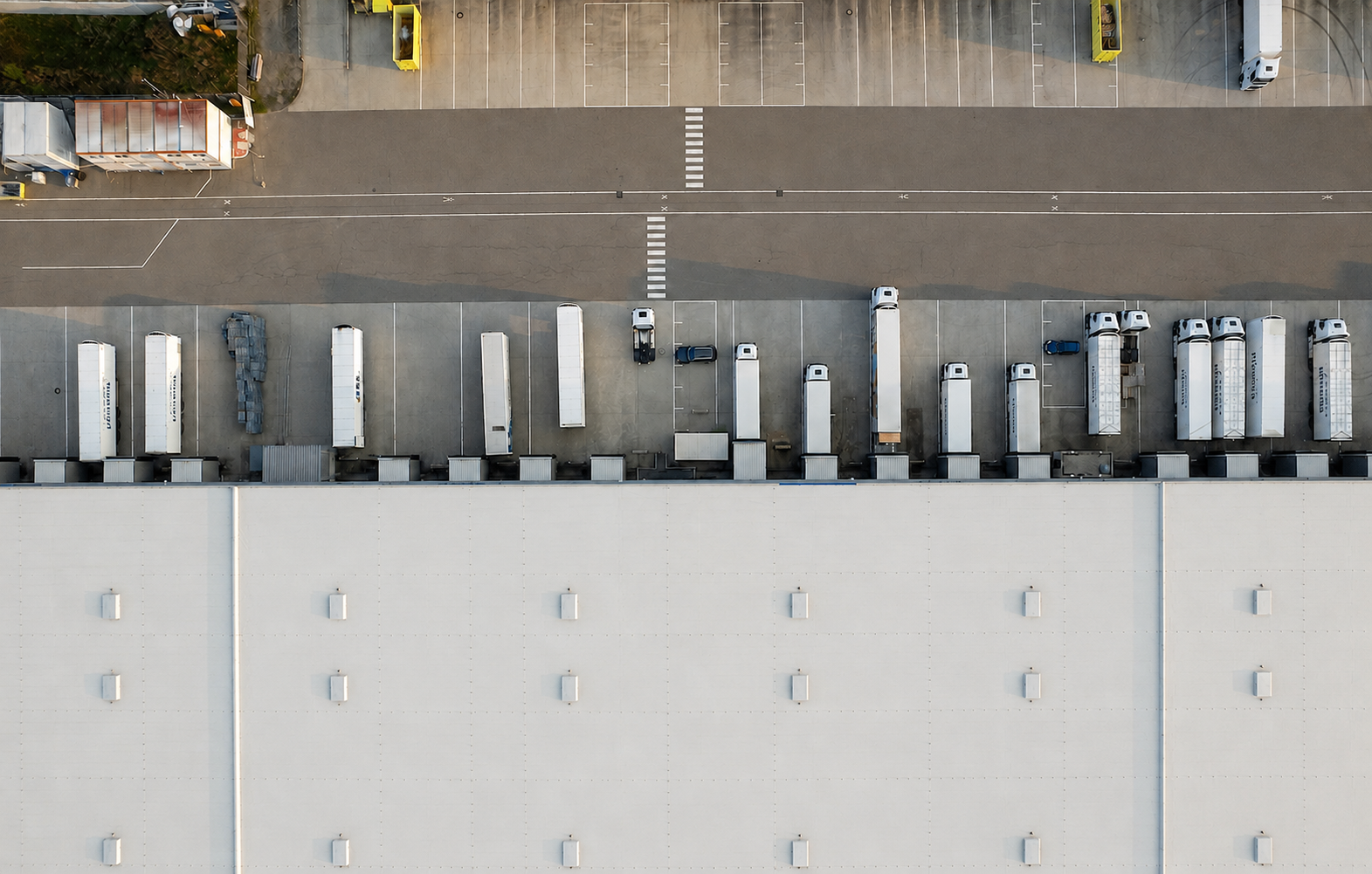 Aerial view of trucks docked at loading bays of a large warehouse building.