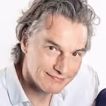 Portrait of Maarten Bennis with light grey hair, light skin and a light blouse, smiling with a light background.