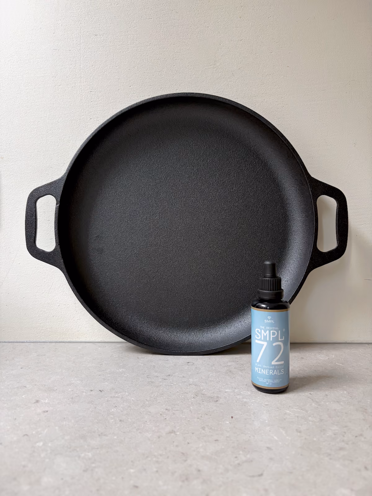 Een flesje SMPL72 met druppelaar naast een glas water op een houten bijzettafel