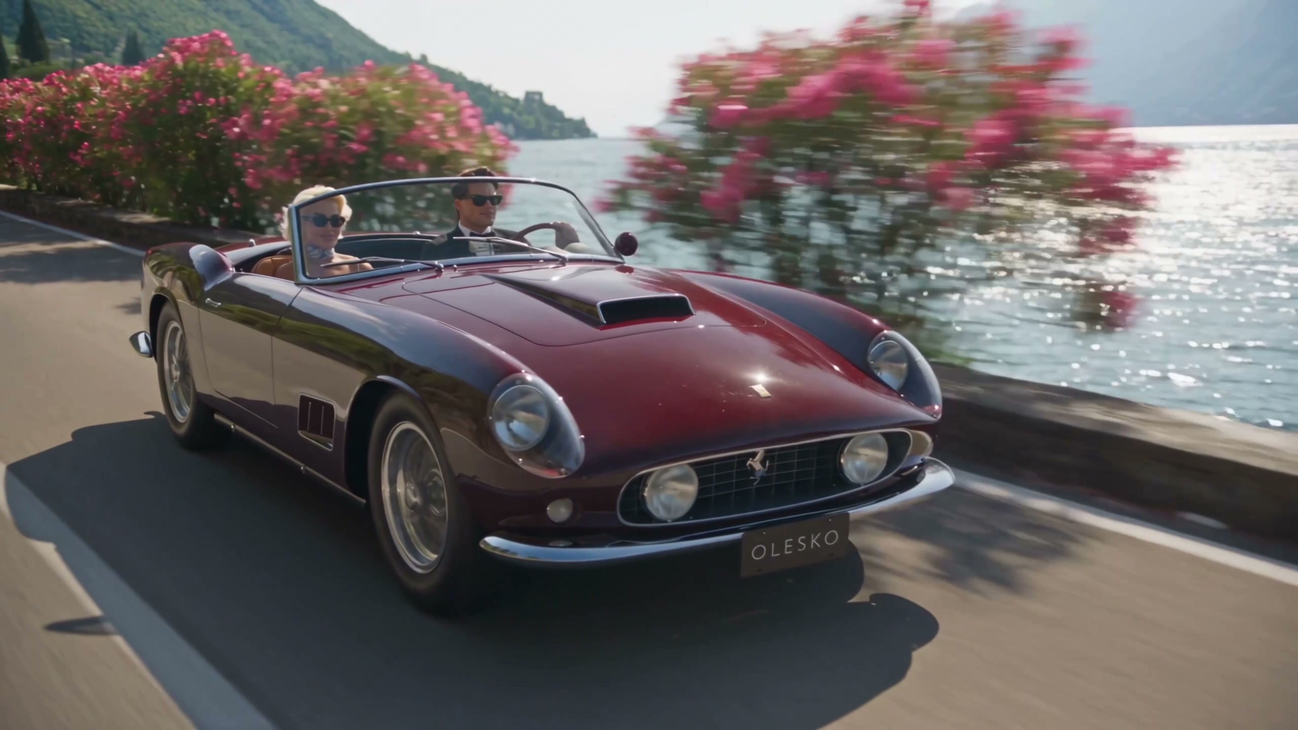 Vintage dark red convertible with an OLESKO plate on a lakeside road