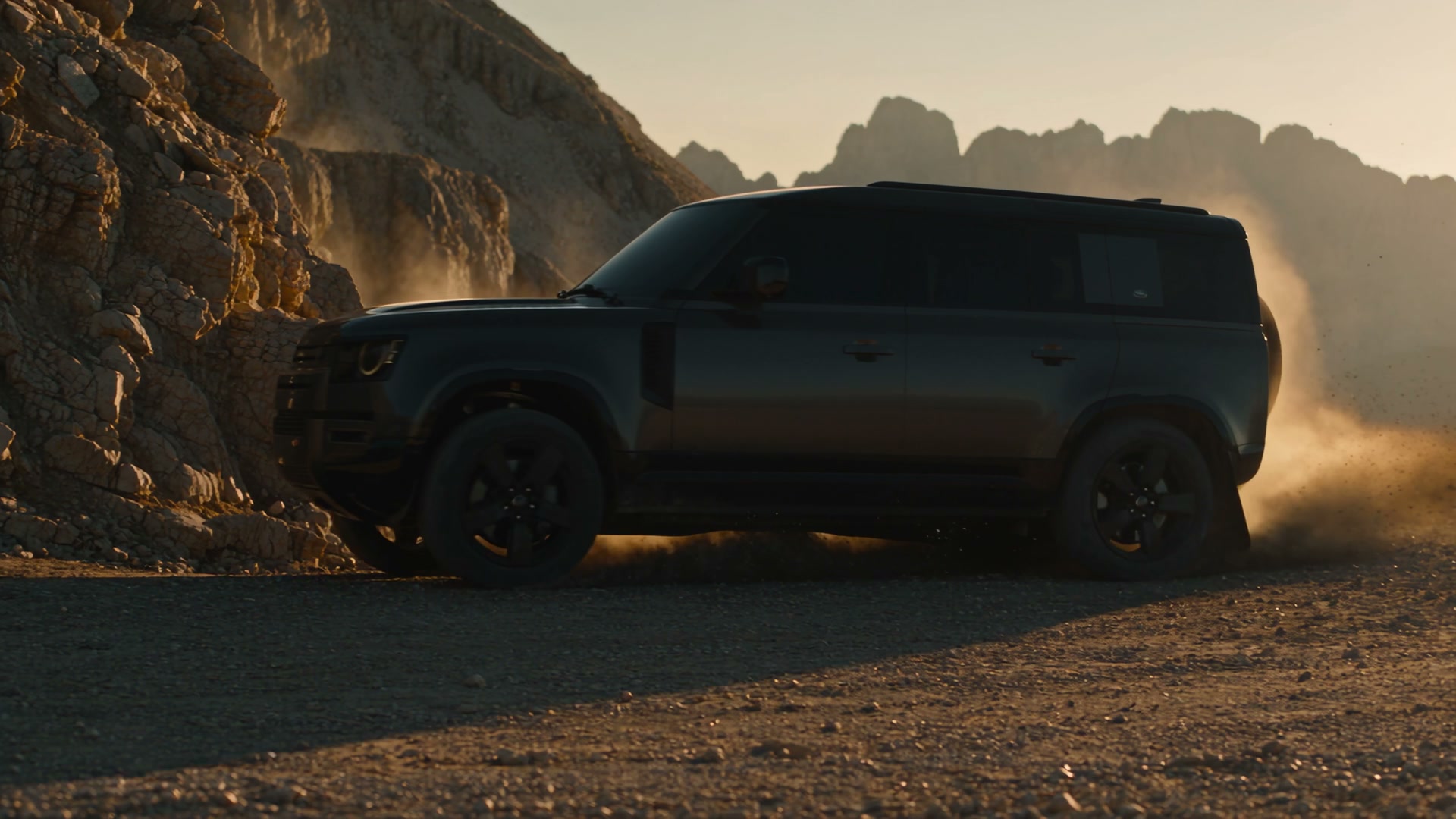 Black Land Rover Defender 110 V8 driving a desert track at golden hour, kicking up dust