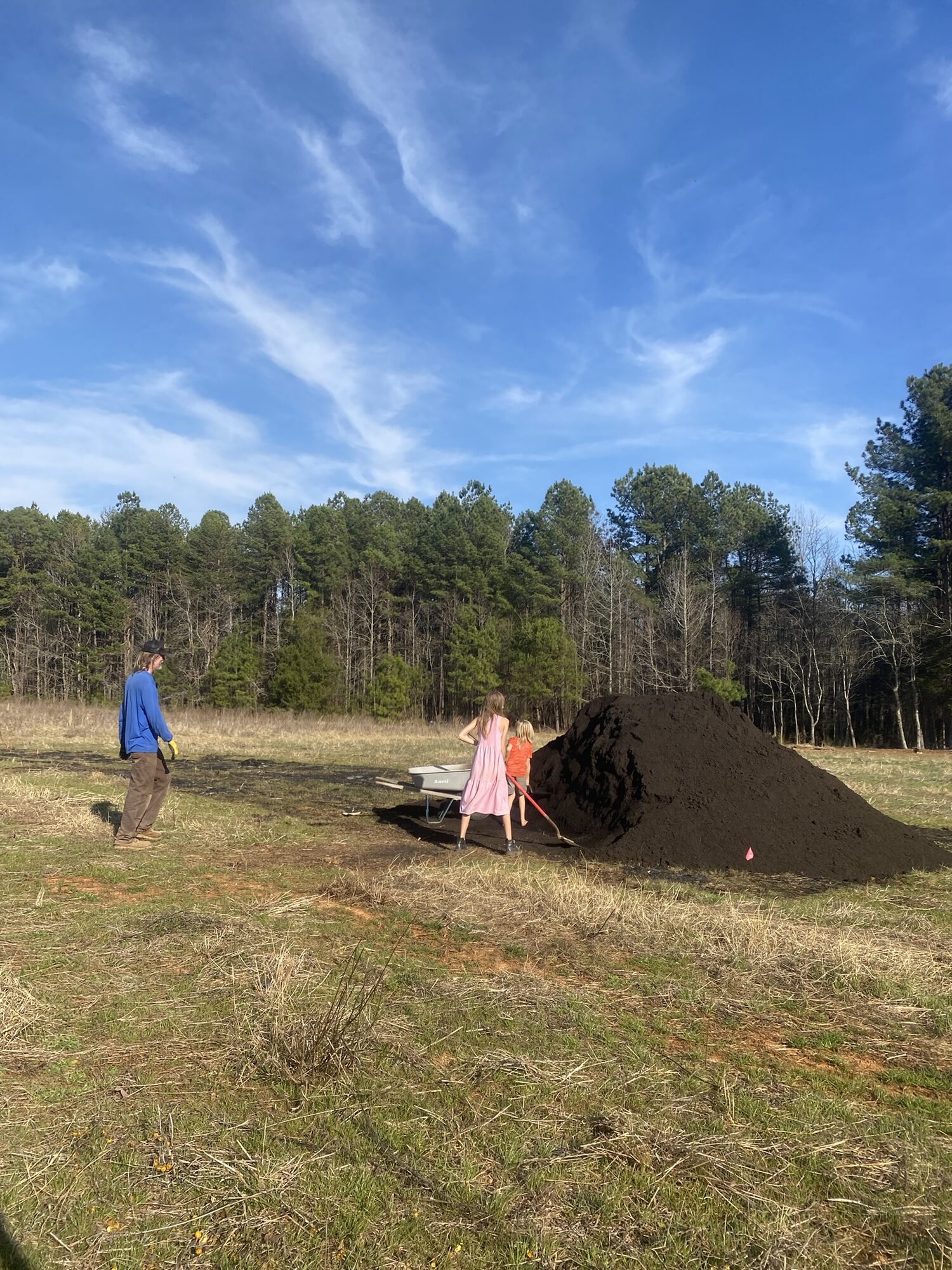 Farmer and child standing beside a large compost pile in a field under a blue sky at Zephyr Family Farm