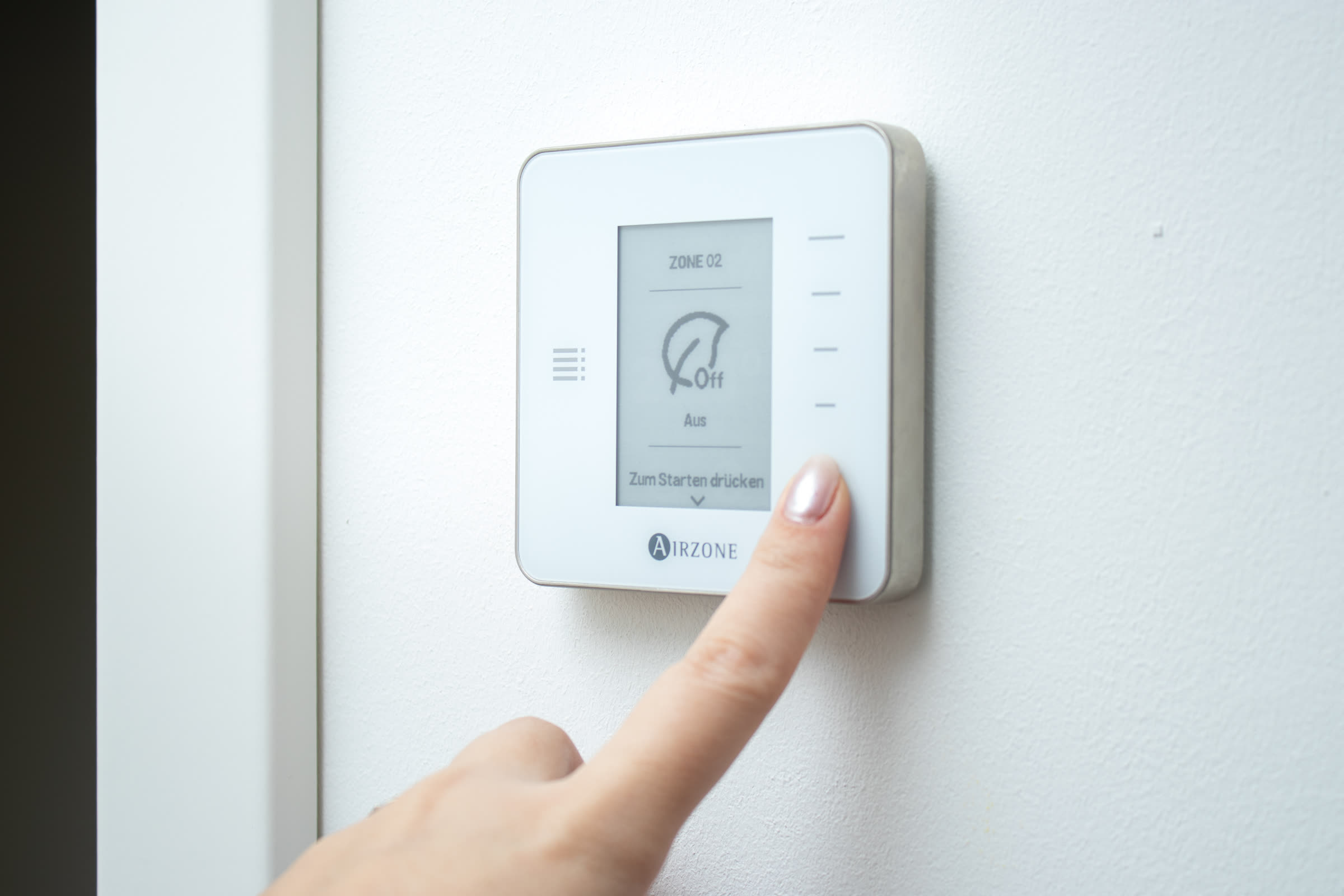 Finger adjusting a modern smart thermostat on a white wall