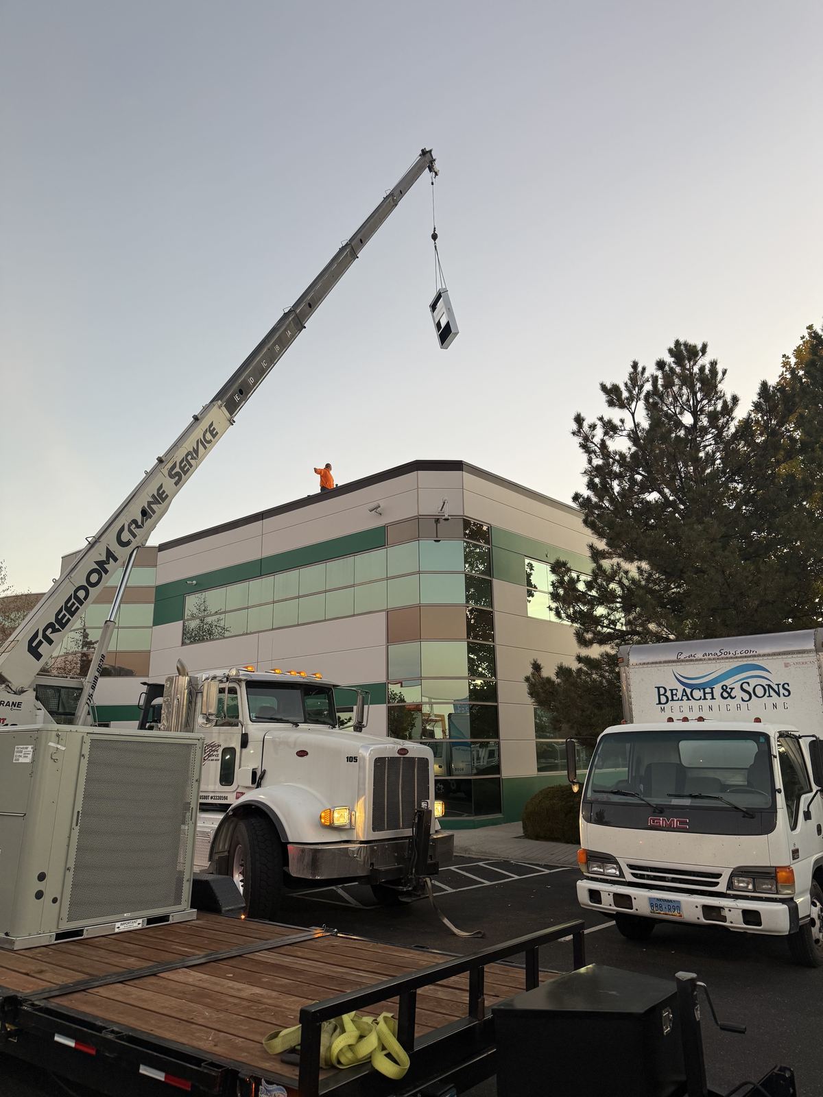 Crane and Beach and Sons trucks staging HVAC equipment at a commercial building