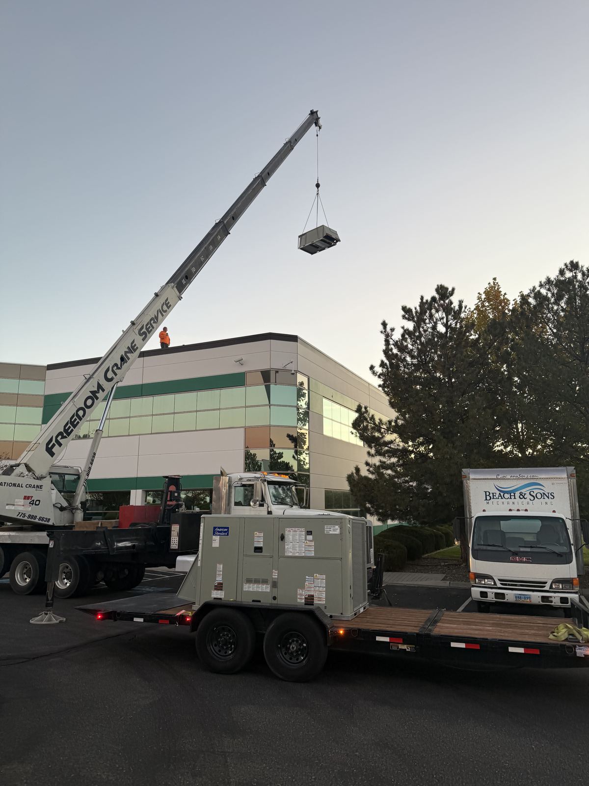 Crane lifting a packaged rooftop HVAC unit from a trailer