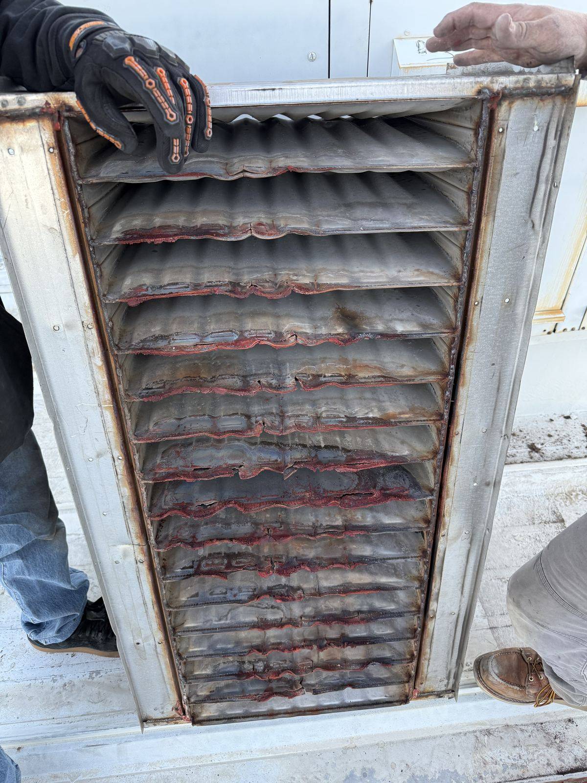 Technician holding a rusted and cracked heat exchanger panel removed from a furnace