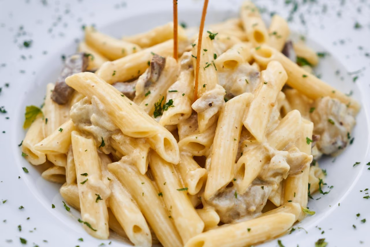 Plate of penne pasta with creamy sauce, mushrooms, and sprinkled herbs.