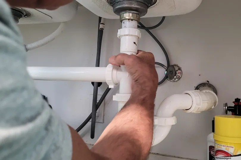 A technician working under a sink to clean the drain.