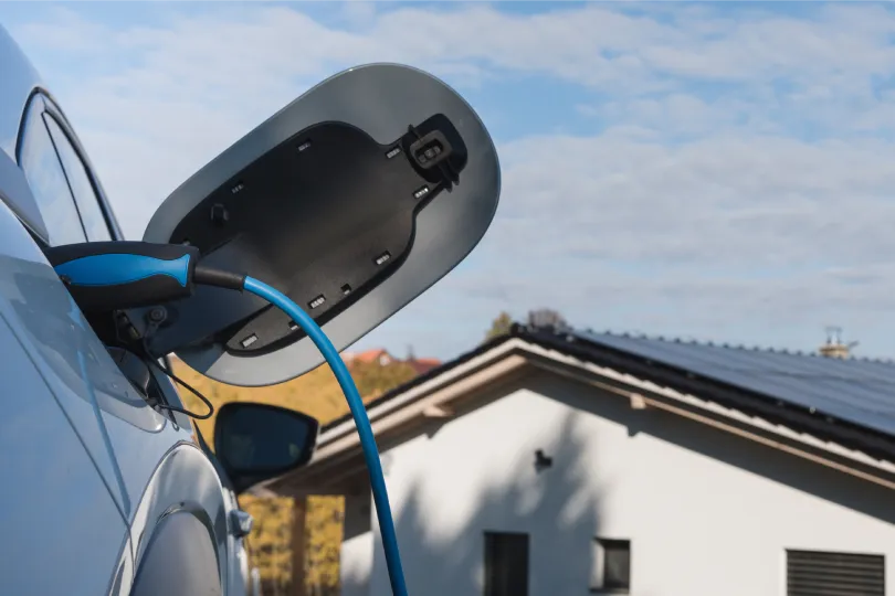 An electric car being charged at home with solar panels on the roof in the background.