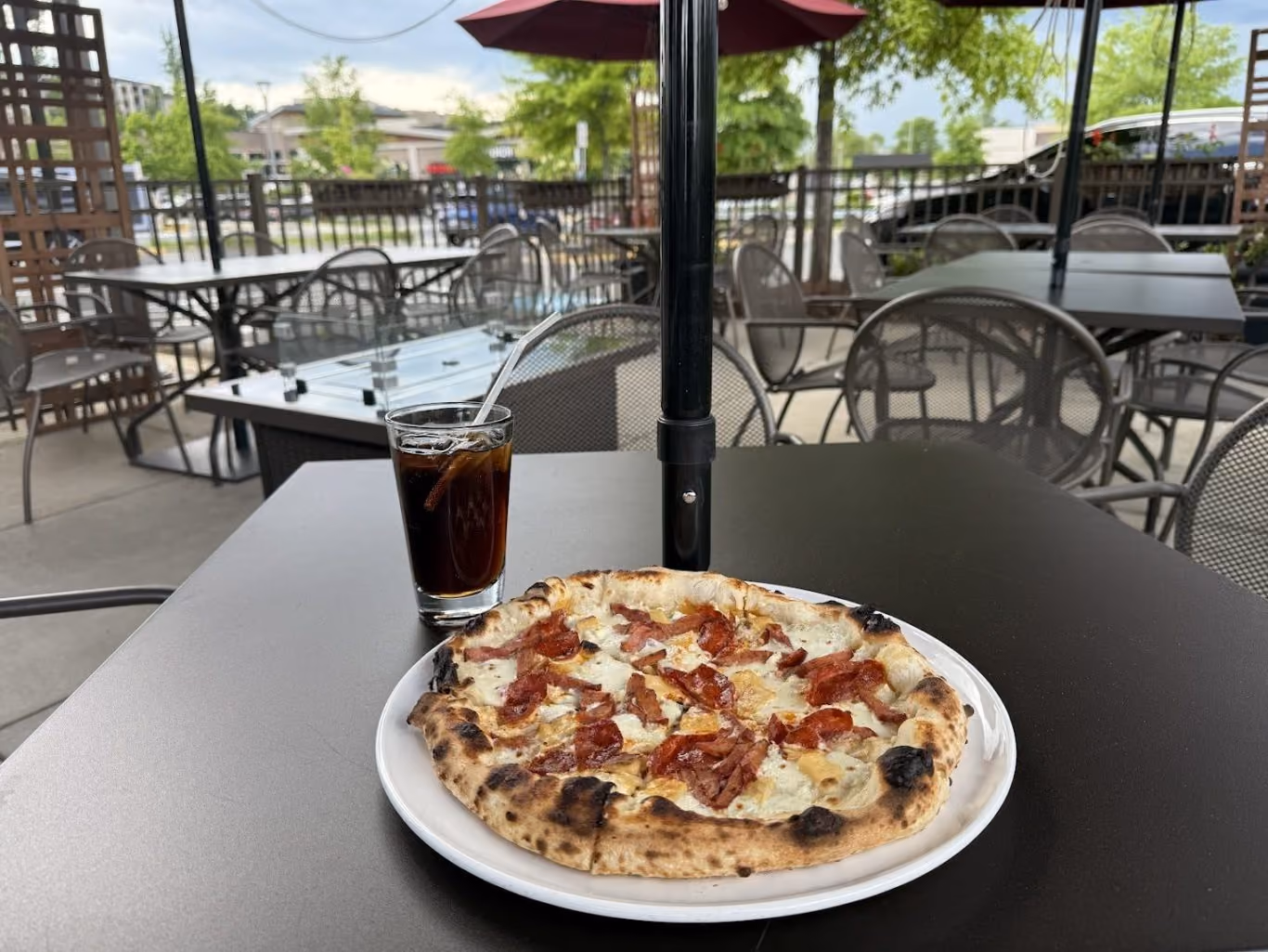 Pepperoni pizza on a white plate with a glass of cola on a dark table at an outdoor patio.