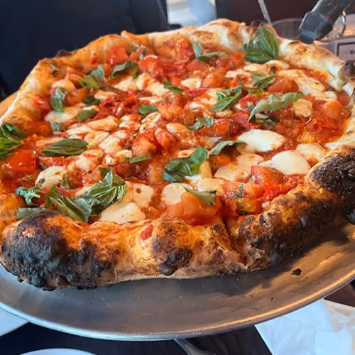 Close-up of a freshly baked pizza with tomato, mozzarella, and basil on a metal tray.