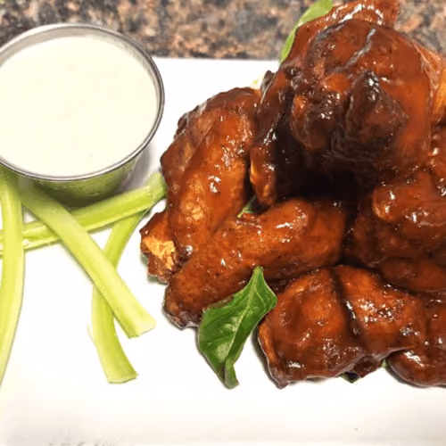 Plate of sauced chicken wings with celery sticks and a cup of ranch dressing.