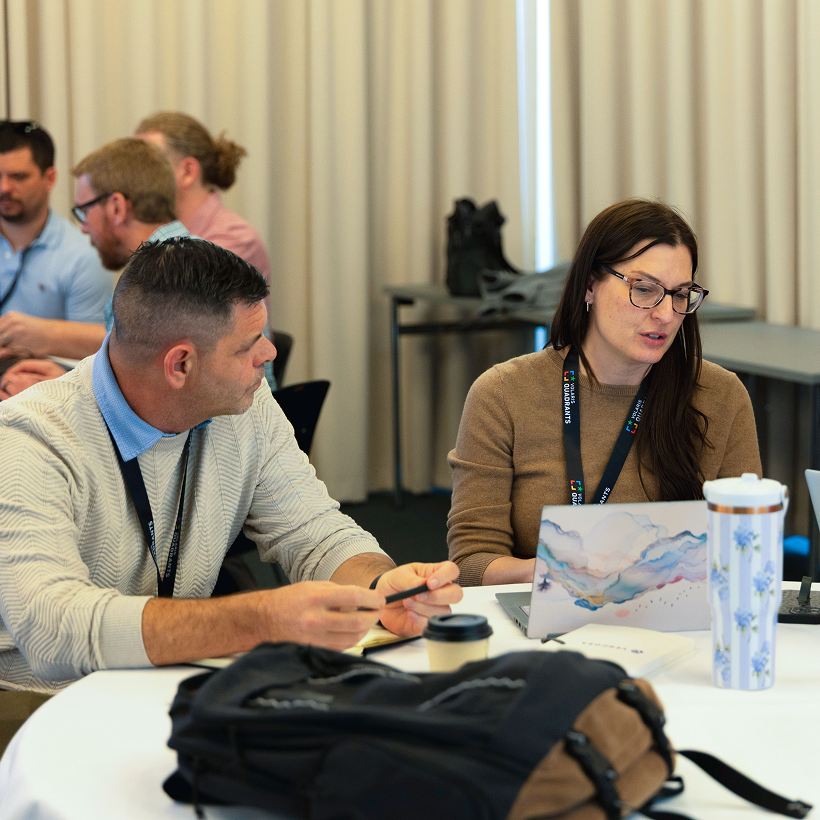 Two conference attendees with lanyards talking at a table
