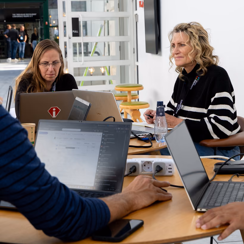 Colleagues working on laptops together at a shared table during a conference