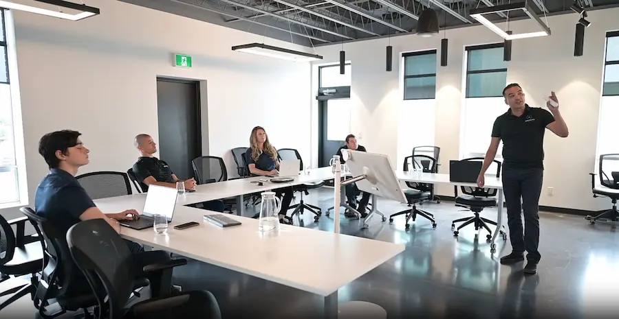 Man standing and speaking to four seated colleagues in a modern office meeting room.