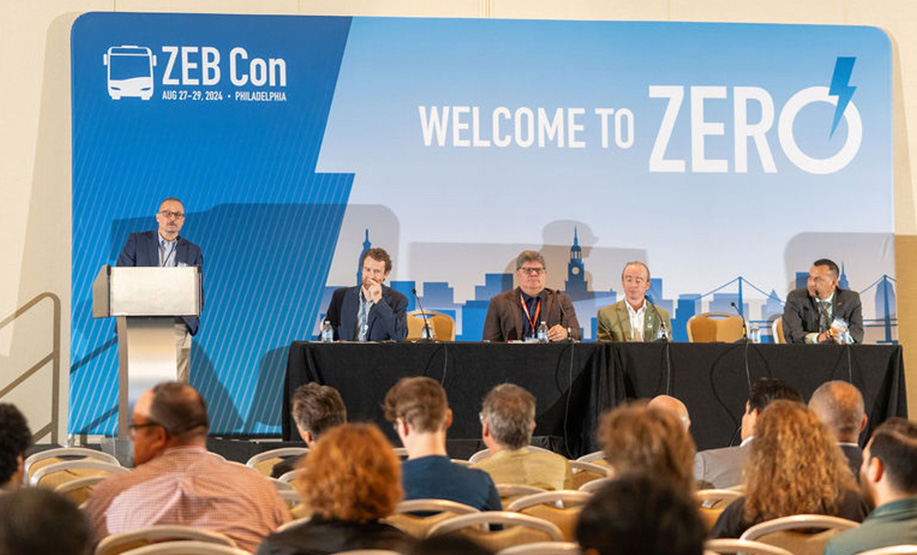 A speaker at a podium and four panelists seated at a table on stage during the ZEB Con conference with a blue backdrop showing 'WELCOME TO ZERO' and event details in Philadelphia, August 27-29, 2024, attended by an audience.