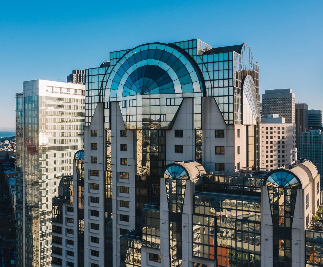 Modern high-rise buildings with distinctive blue-tinted glass architectural designs under a clear blue sky in an urban setting.