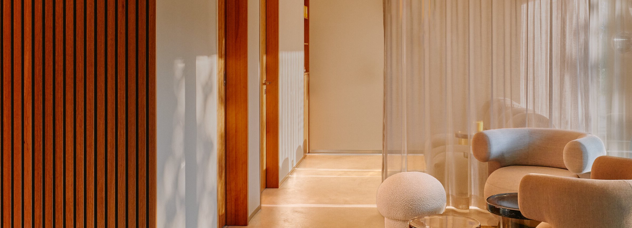 A calm, sunlit waiting area with armchairs and a slatted wood wall