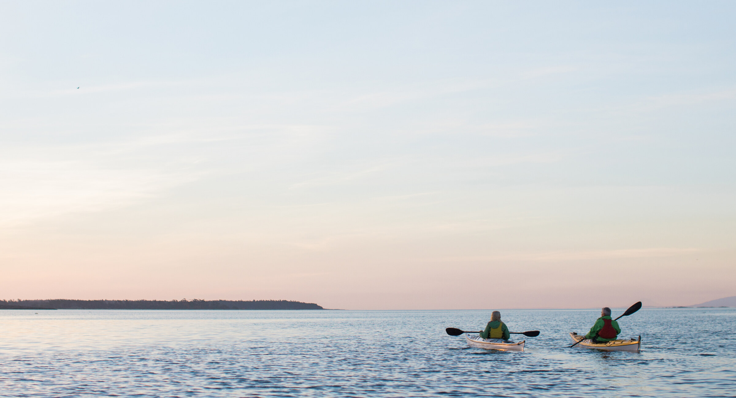 Two people kayaking on calm water at sunset