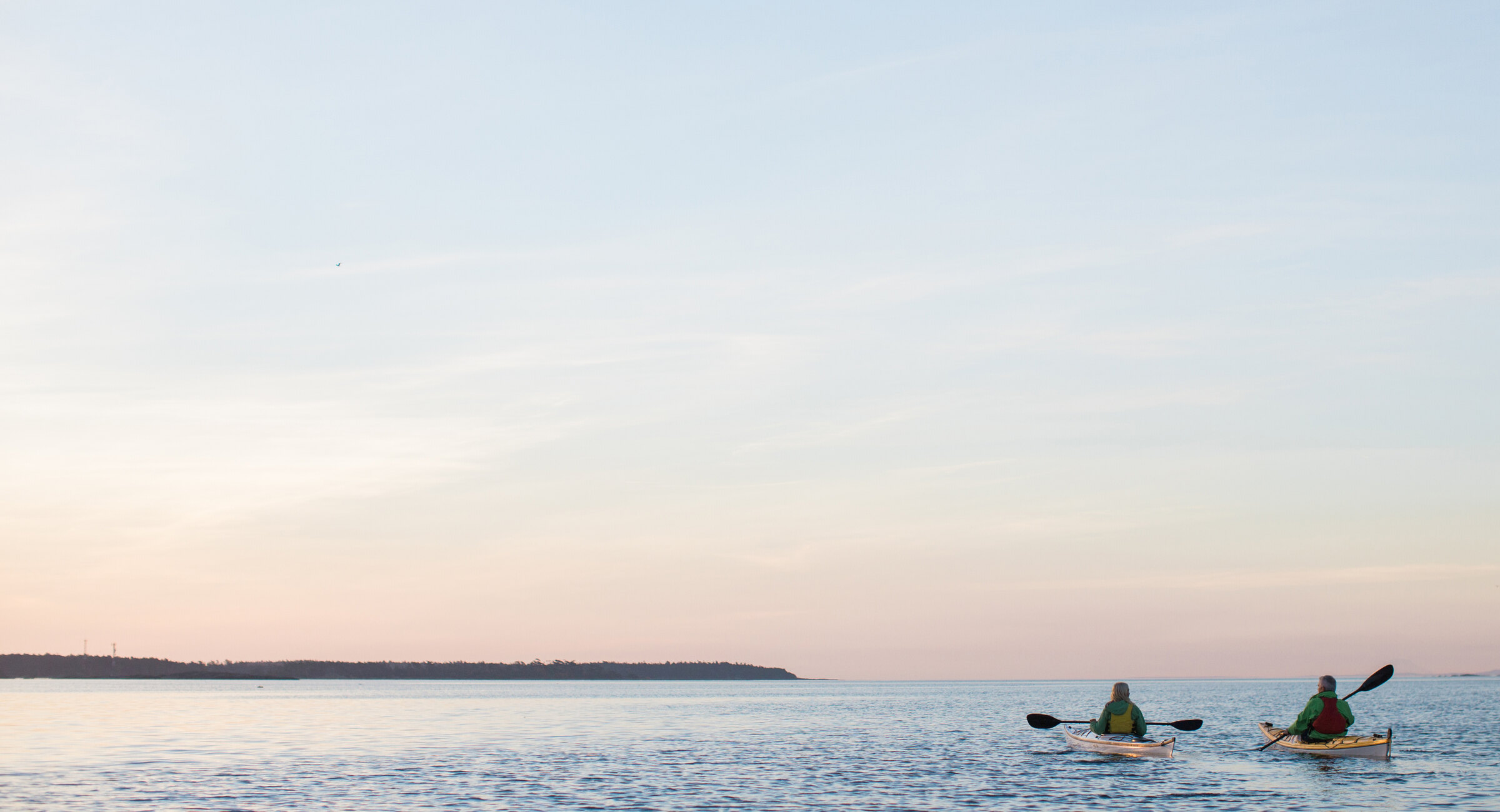 Two people kayaking on calm water at sunset