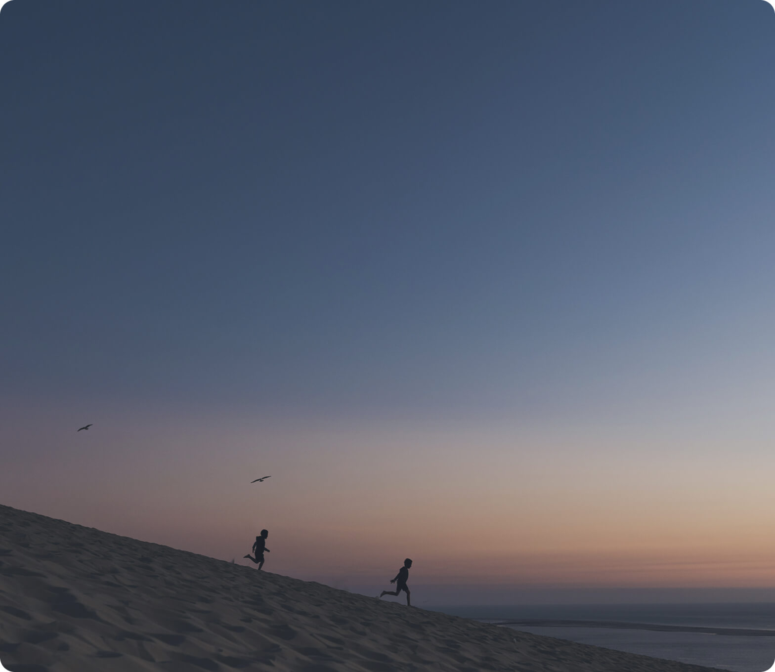 Two people running along a sand dune at sunset