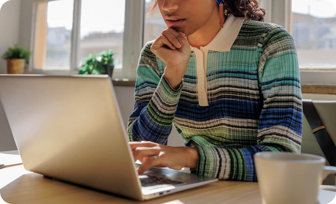 A woman at a kitchen table looking at her laptop