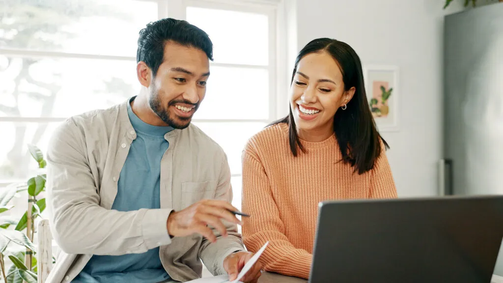 A smiling couple reviewing paperwork together at a laptop