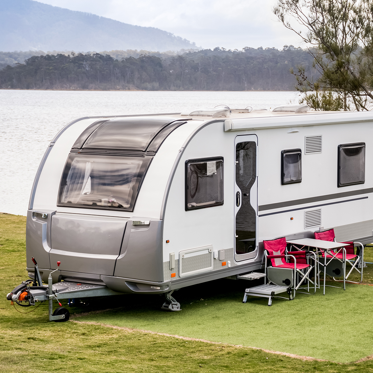 Caravan parked beside a peaceful Australian lake with mountains in the distance