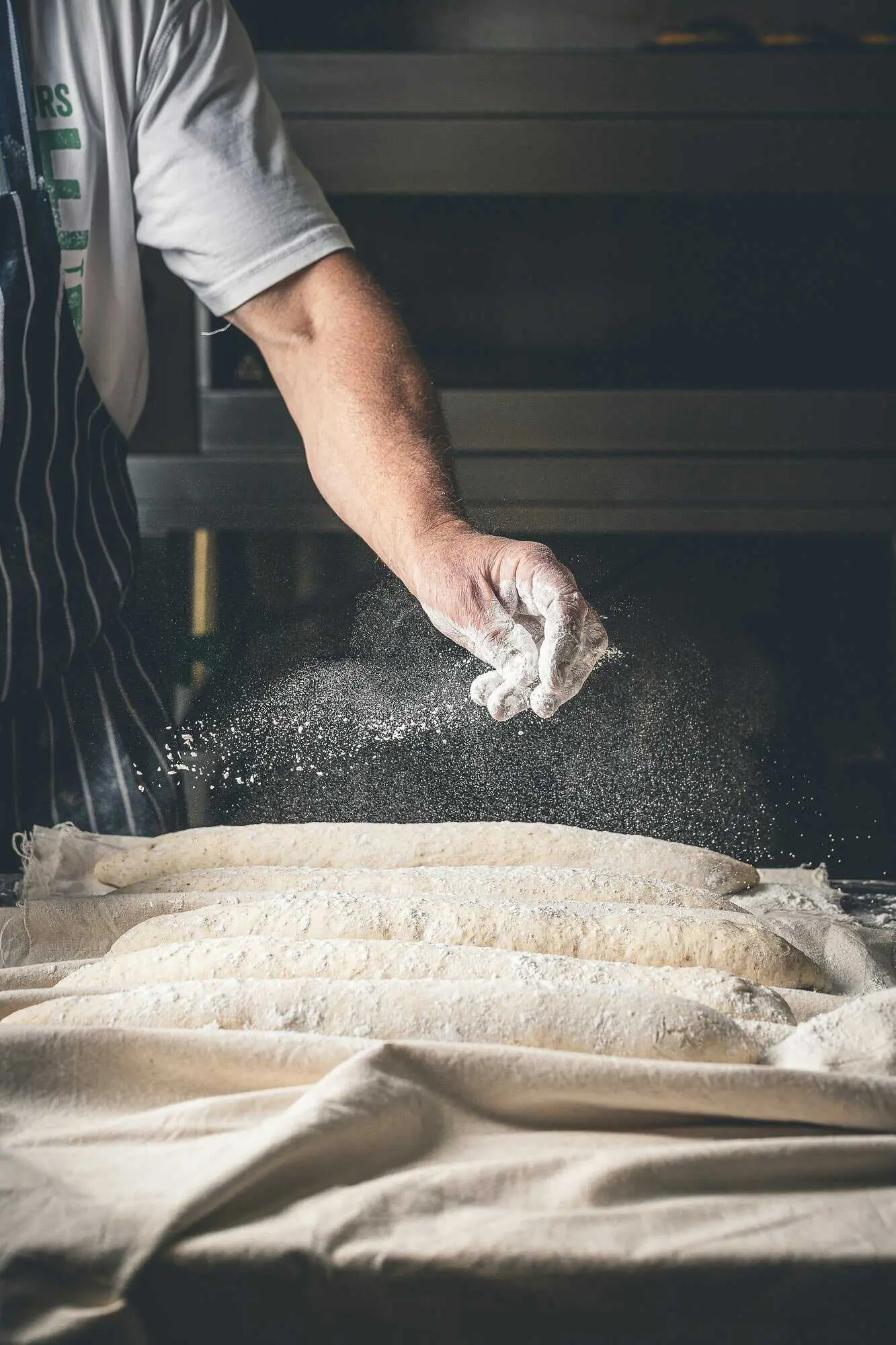 A baker dusting flour over shaped loaves before baking