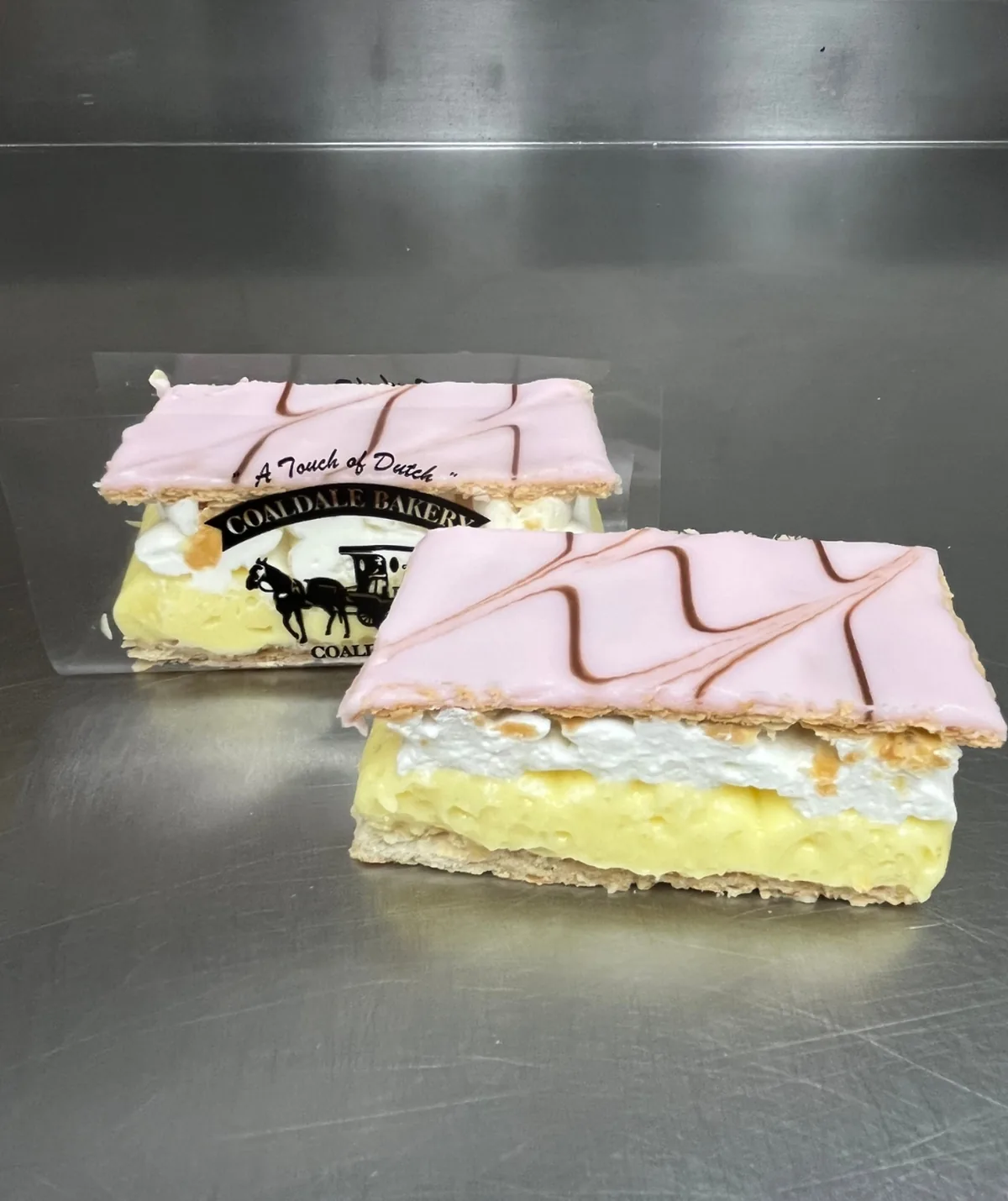 A vanilla slice with pink icing, showing the custard and cream layers