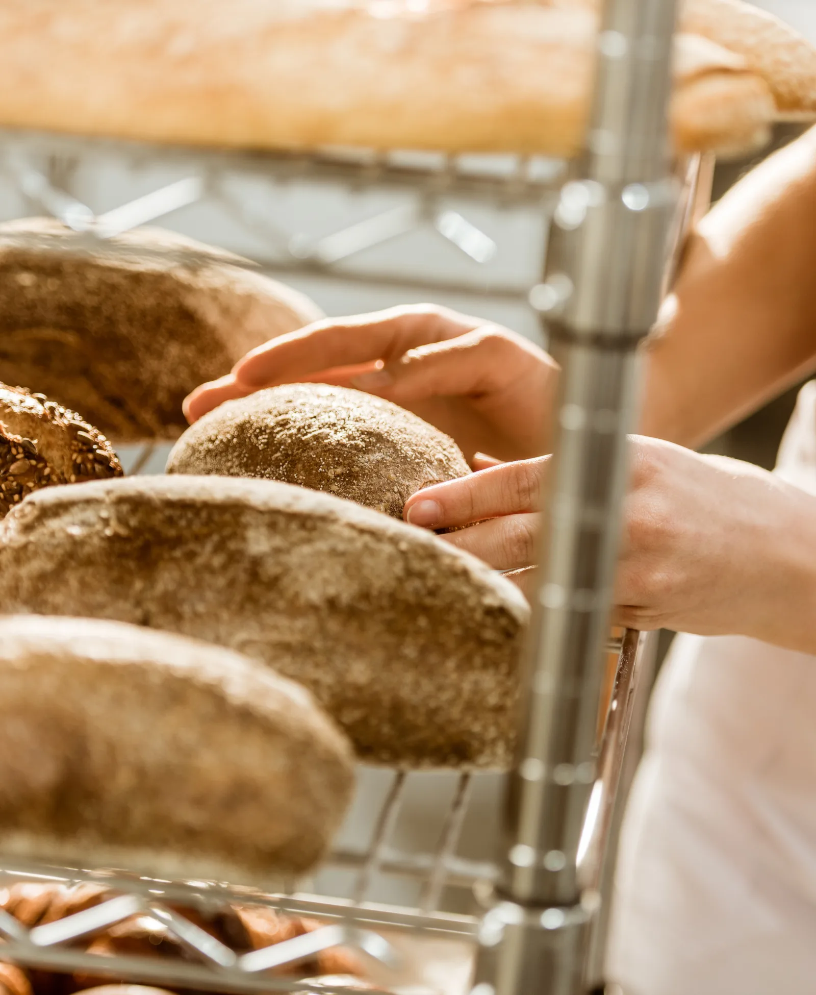 A baker arranging fresh loaves of bread on a bakery display rack
