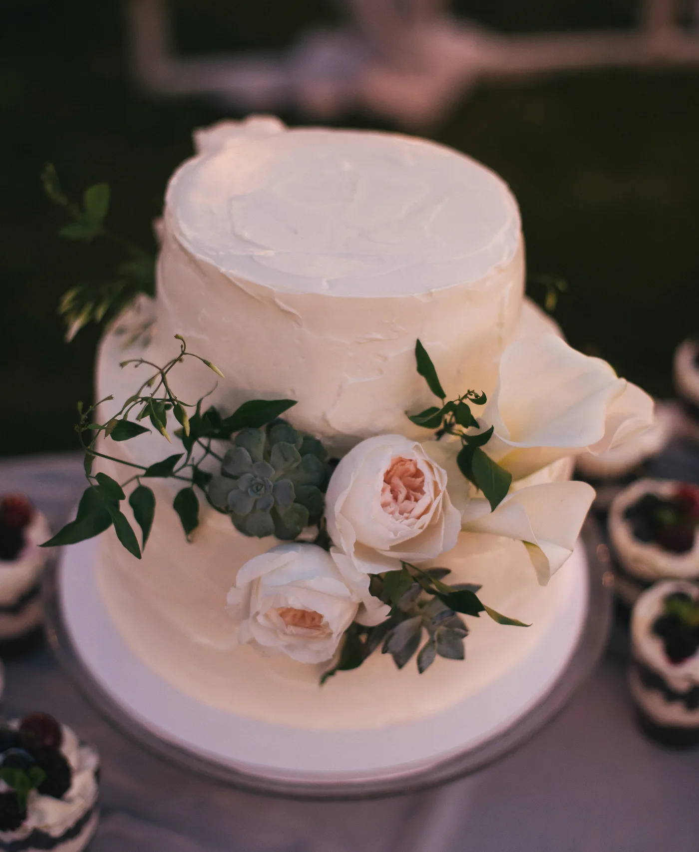 A two tier white buttercream wedding cake decorated with roses and greenery