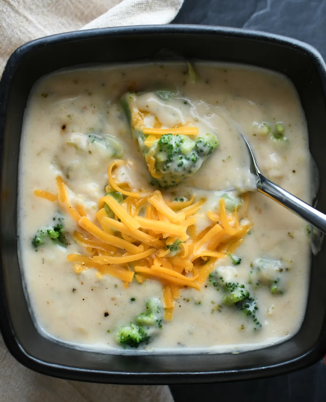A bowl of broccoli cheddar soup topped with shredded cheese