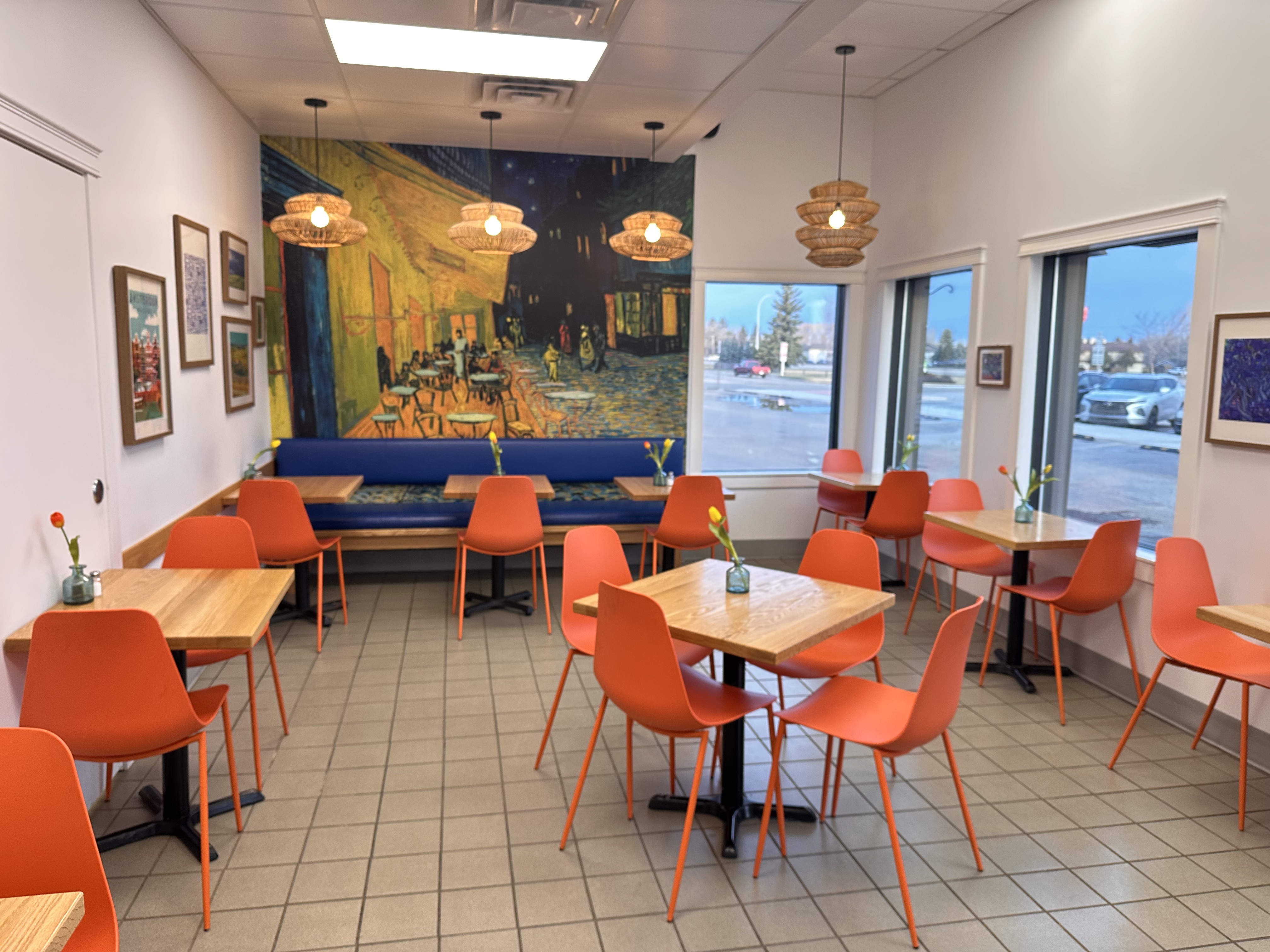 Inside Coaldale Bakery, orange chairs and wooden tables in the seating area beside a painted mural