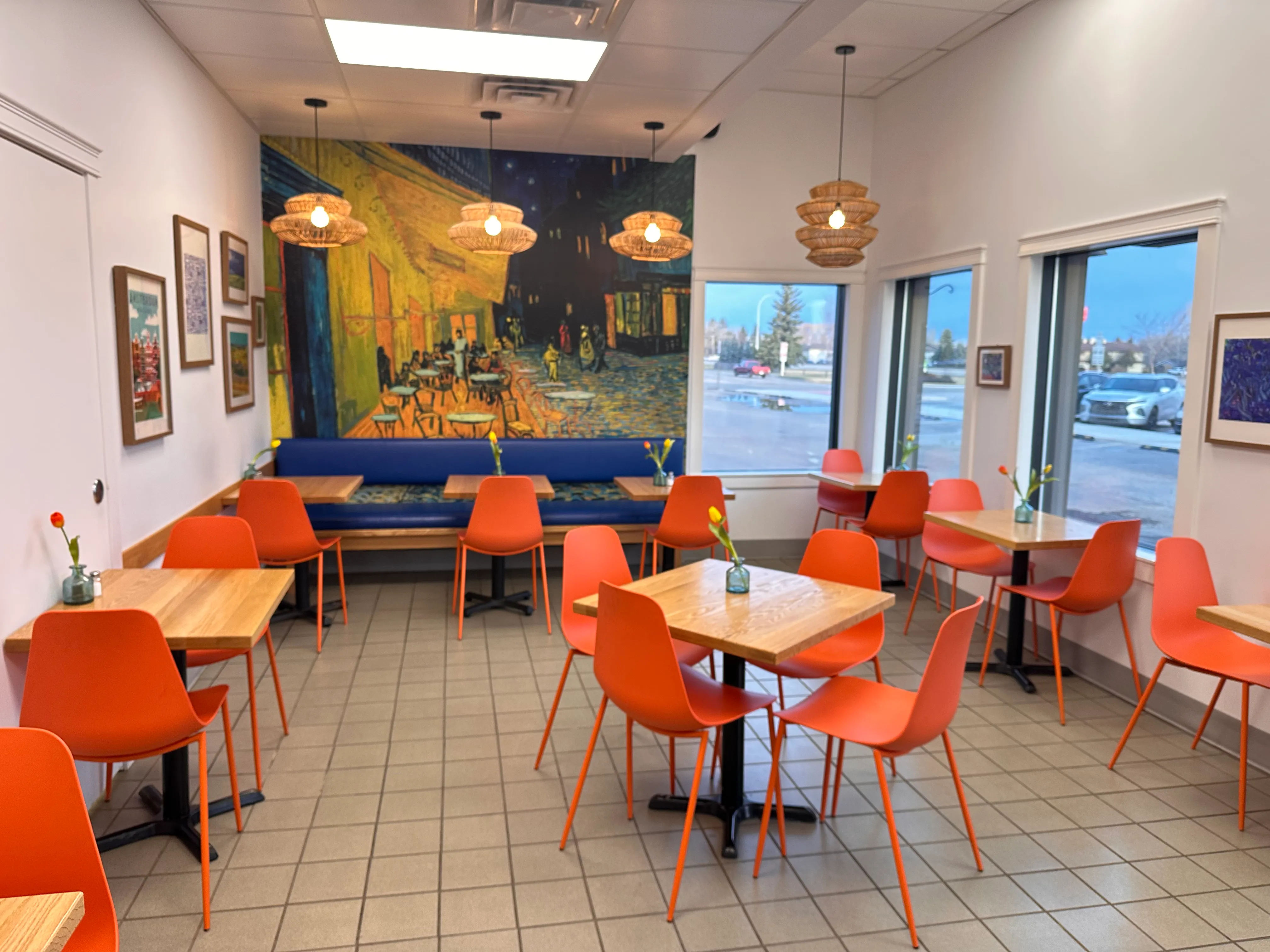 Inside Coaldale Bakery, orange chairs and wooden tables in the seating area beside a painted mural