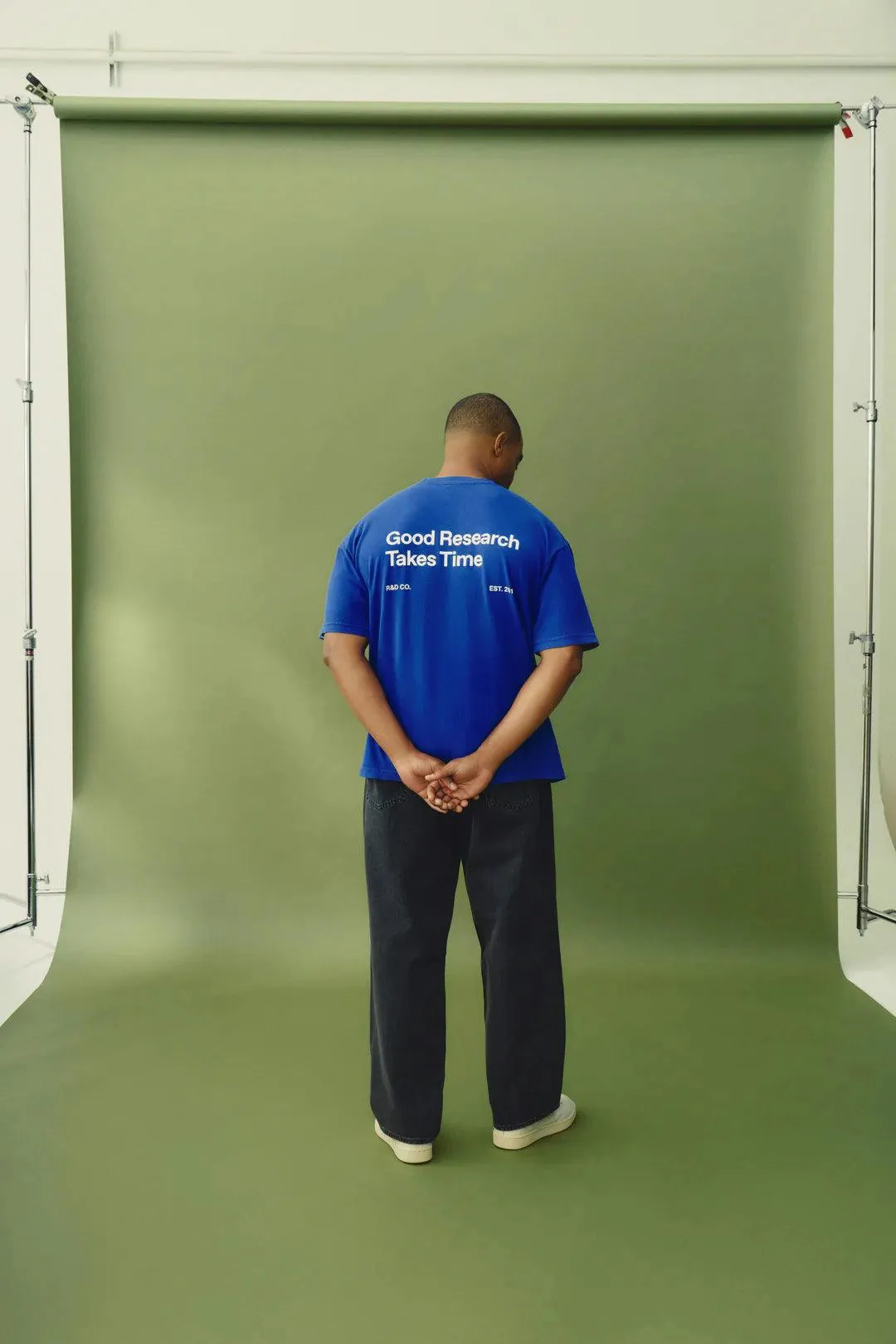 Man in blue oversized t-shirt with 'Good Research Takes Time' printed on the back, styled as startup swag