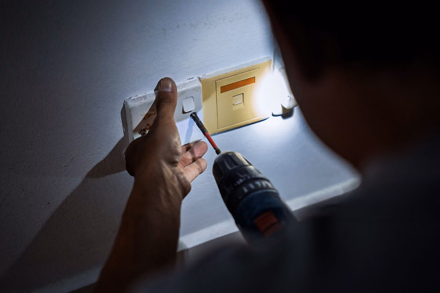 Person using a drill to install or repair a wall switch or electrical outlet plate at night.