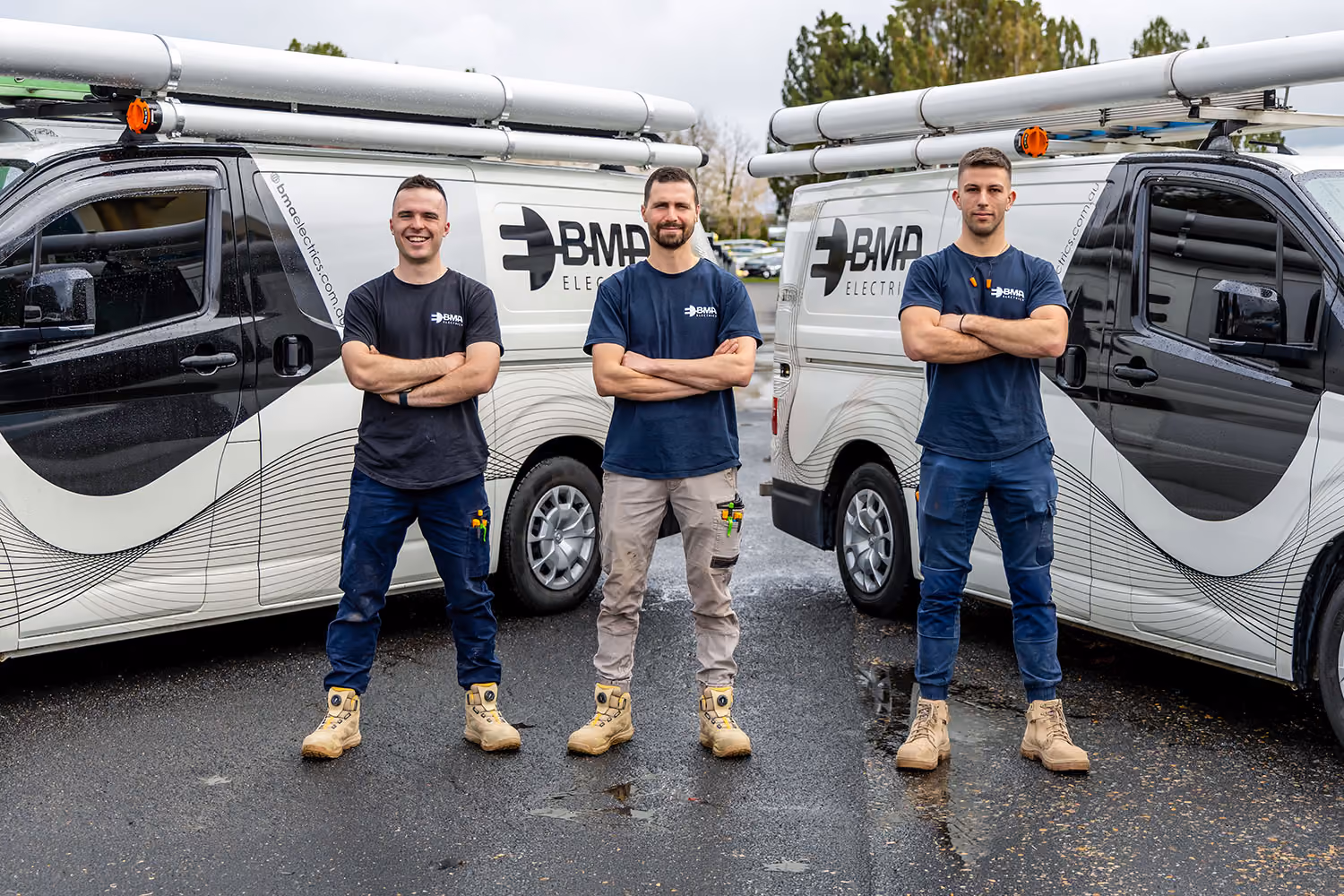 Three electricians standing with arms crossed in front of vans with BMA Electrics logos.