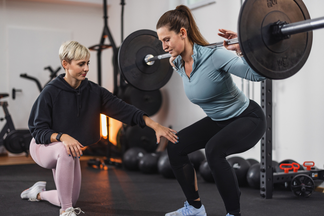 Female strength coach guiding a woman through a loaded barbell squat